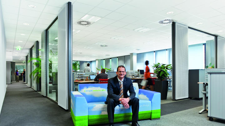 Seorang pria duduk di sofa berdesain langit di koridor kantor Audi yang diterangi dengan pencahayaan Philips