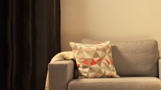 Ruang tamu yang nyaman dengan lampu meja LED modern, menerangi sofa panjang abu-abu dan menciptakan suasana hangat untuk bersantai di rumah.