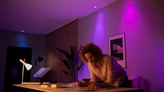 Lampu LED pintar Philips Hue menciptakan suasana ungu dan merah muda yang cerah di ruang keluarga, menampilkan pencahayaan suasana hati yang dapat disesuaikan untuk malam menonton film dan bersantai di rumah modern.