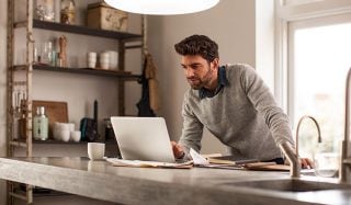 Pria menggunakan laptop di kantor rumah yang cukup terang dengan lampu kerja LED untuk pengaturan kerja jarak jauh yang efisien.