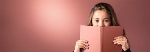 "Gadis muda mengintip buku berwarna merah muda dengan latar belakang lampu LED lembut, menampilkan pencahayaan yang hangat dan merata untuk lingkungan membaca yang nyaman."