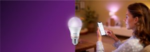 "Wanita mengendalikan lampu LED pintar melalui aplikasi telepon pintar, menciptakan suasana hangat di ruang tamu yang nyaman dengan teknologi rumah yang terhubung."